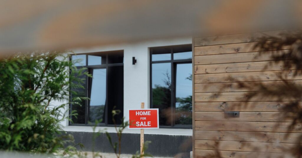A contemporary home with a 'For Sale' sign in the front yard, framed by greenery.