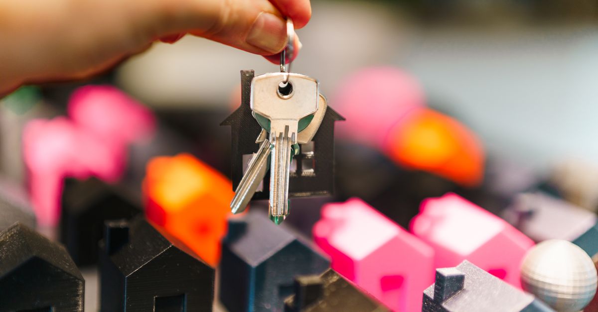 Colorful miniature houses and a hand holding keys representing real estate decisions.