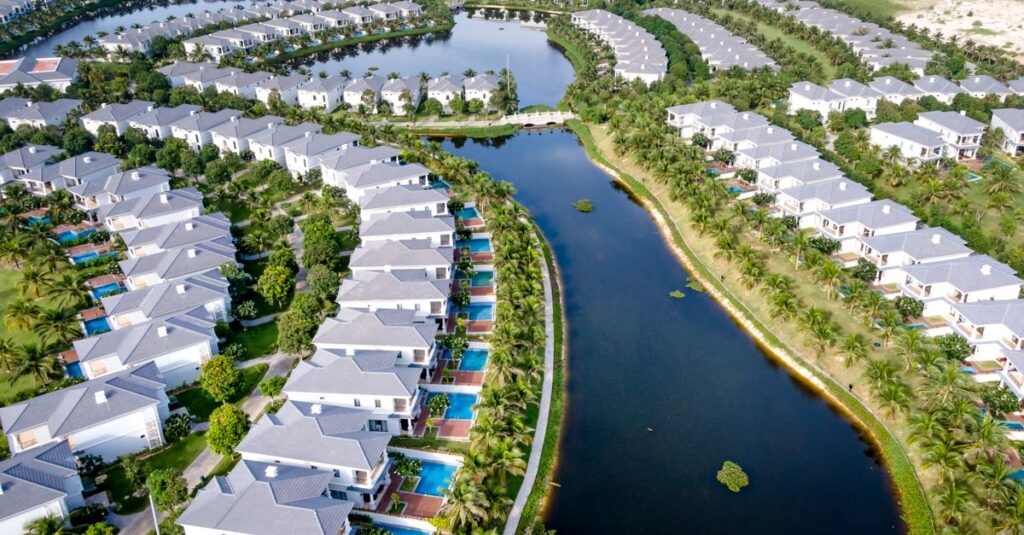 Stunning aerial view of tropical villas with pools overlooking a serene lagoon, ideal for vacation and leisure.