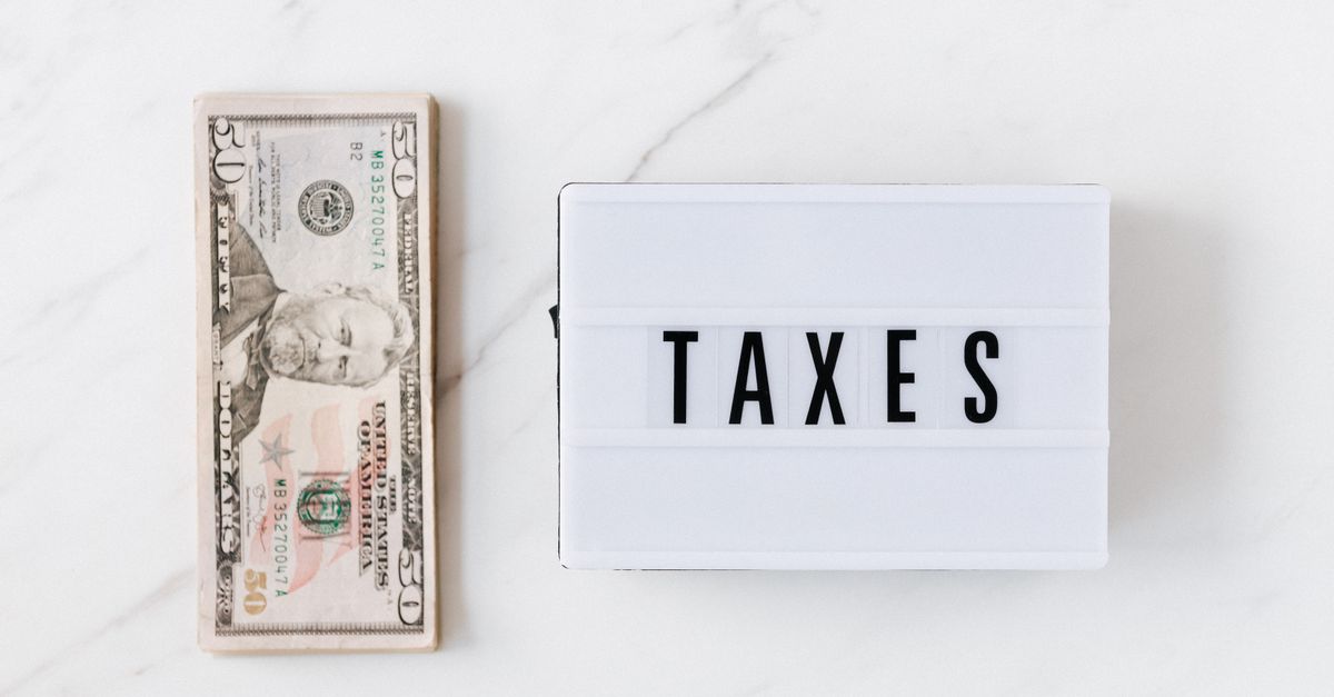 Top view composition of stack of American dollars placed on white marble surface with white retro light box with TAXES inscription