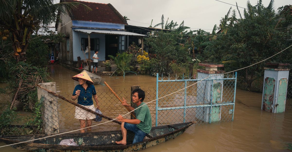 Residents navigate floodwaters in Phú Yên, Vietnam, using a small wooden boat.