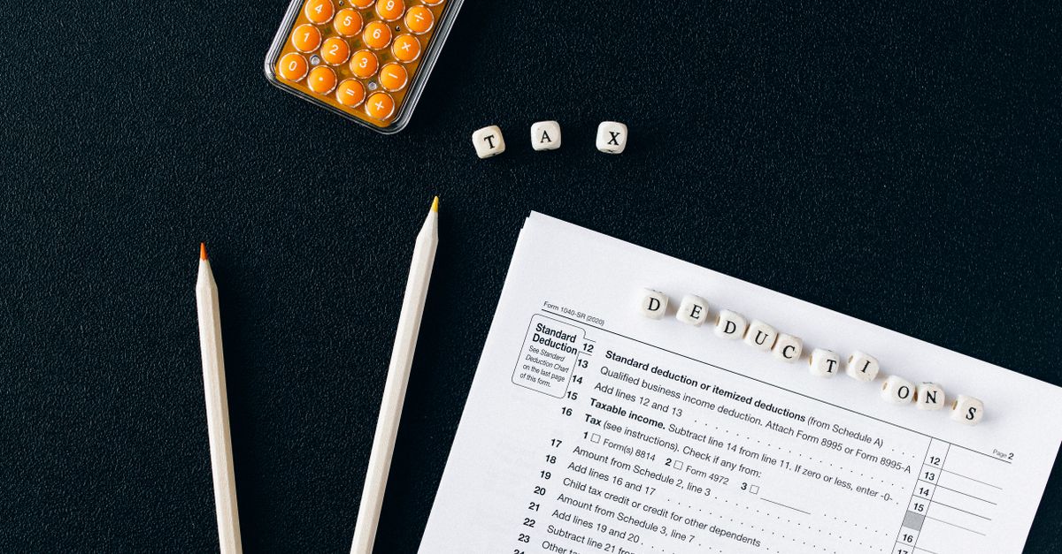Flat lay of tax form, pencils, and calculator on black background, emphasizing tax deductions.
