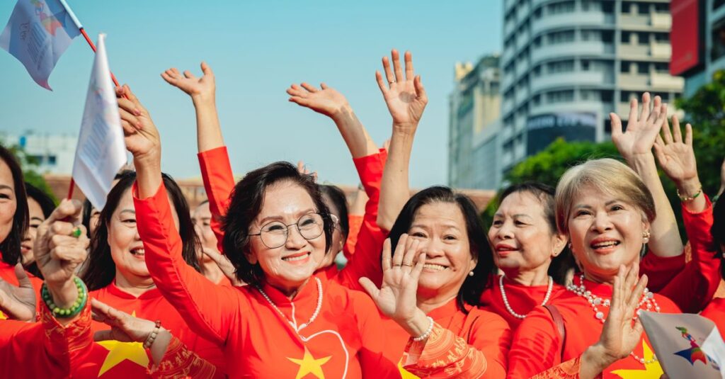 Group of women in red, waving flags, celebrating outdoors with buildings in the background.