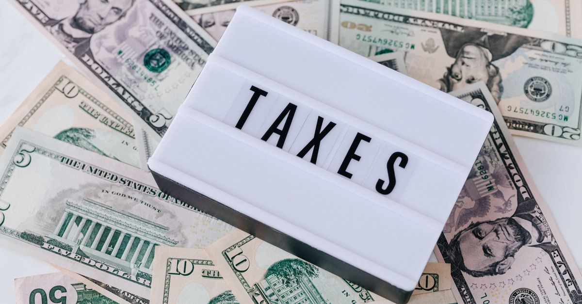 From above of white retro lightbox with TAXES inscription placed on pile of USA dollar bills on white surface