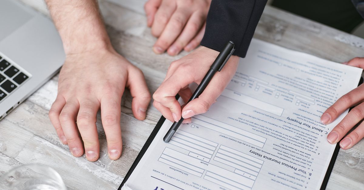 Close-up image of two people signing an insurance policy document on a wooden desk.