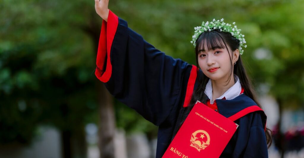Smiling graduate raising hand with diploma outdoors, celebrating achievement.