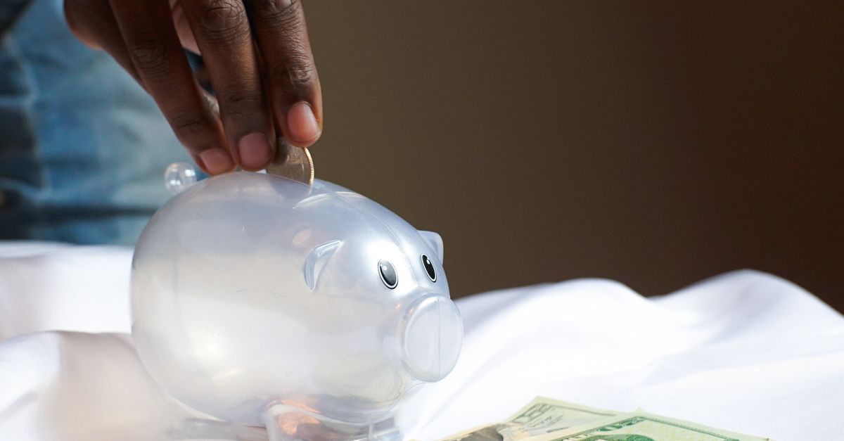 A hand placing a coin in a piggy bank with dollar bills nearby signifying savings and finance.