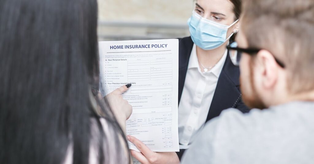 A professional woman explains a home insurance policy to clients during a meeting. Indoors setting.