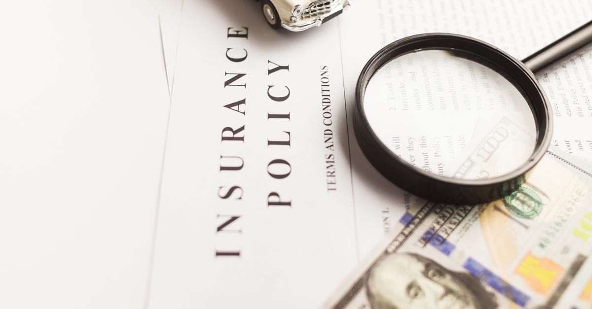 Close-up image of an insurance policy with a magnifying glass, money, and toy car.