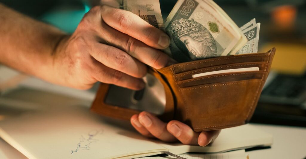 A close-up of hands holding a wallet filled with Polish banknotes on a desk.