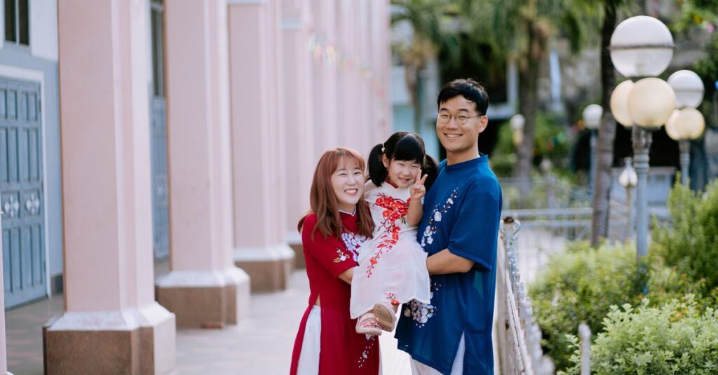 Smiling Asian family in traditional ao dai, enjoying a sunny day outdoors.