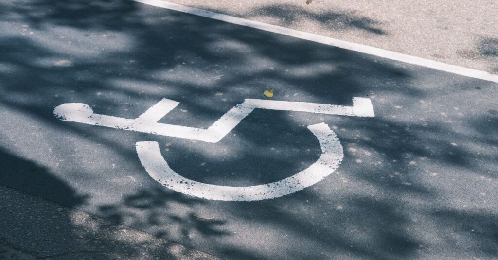 Close-up of an accessible parking symbol on a sunlit asphalt road.