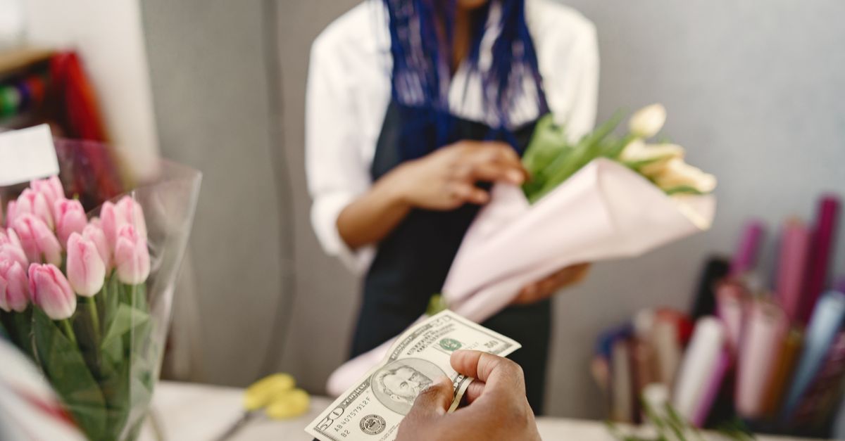 Close-up of a customer paying with cash at a flower shop, handing money to a florist holding a bouquet.