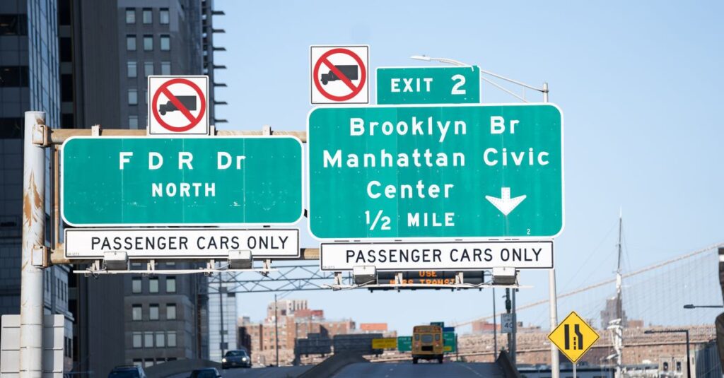 Traffic signs leading to Brooklyn Bridge in New York City on a clear day.