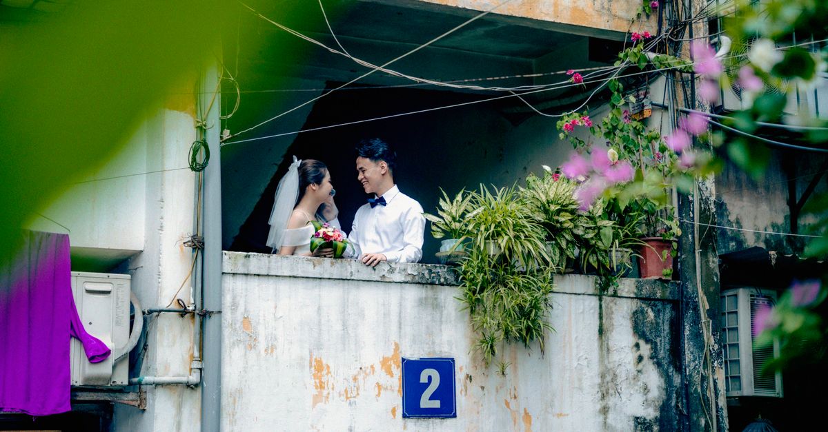Couple in wedding attire sharing a moment on a rustic balcony surrounded by greenery.