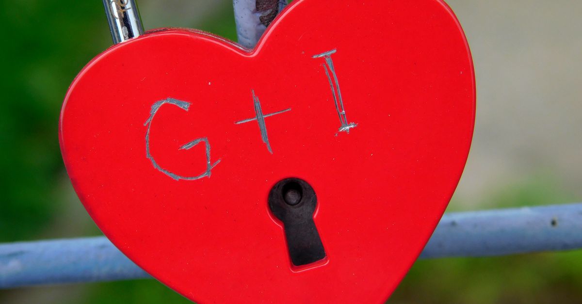 A red heart-shaped padlock symbolizes love and commitment, attached to a metal fence outdoors.