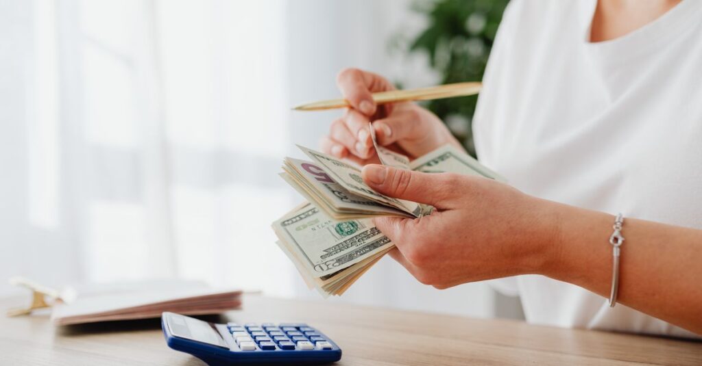 Close-up of a woman holding US dollars, calculating finances at home.