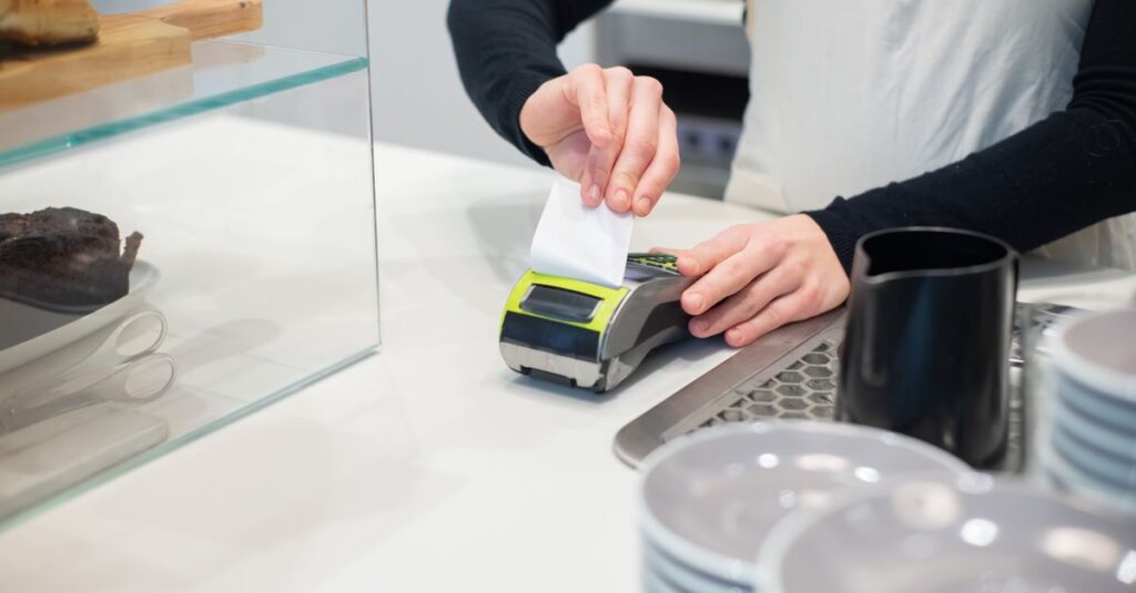 Close-up of a cashless transaction at a modern café counter with hands holding a receipt.