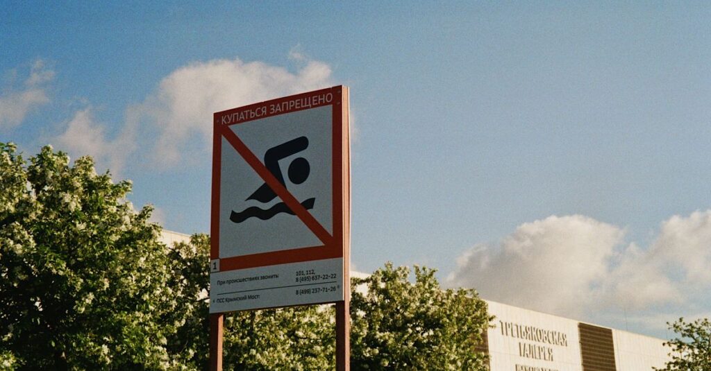 A warning sign prohibiting swimming against a backdrop of trees and a clear blue sky.