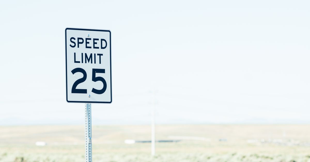 White sign on roadside with speed limit against empty green field at daytime