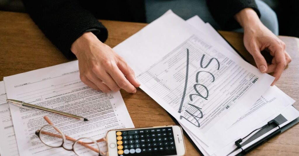 Hands of a person examining tax forms labeled as scam with calculator and papers.