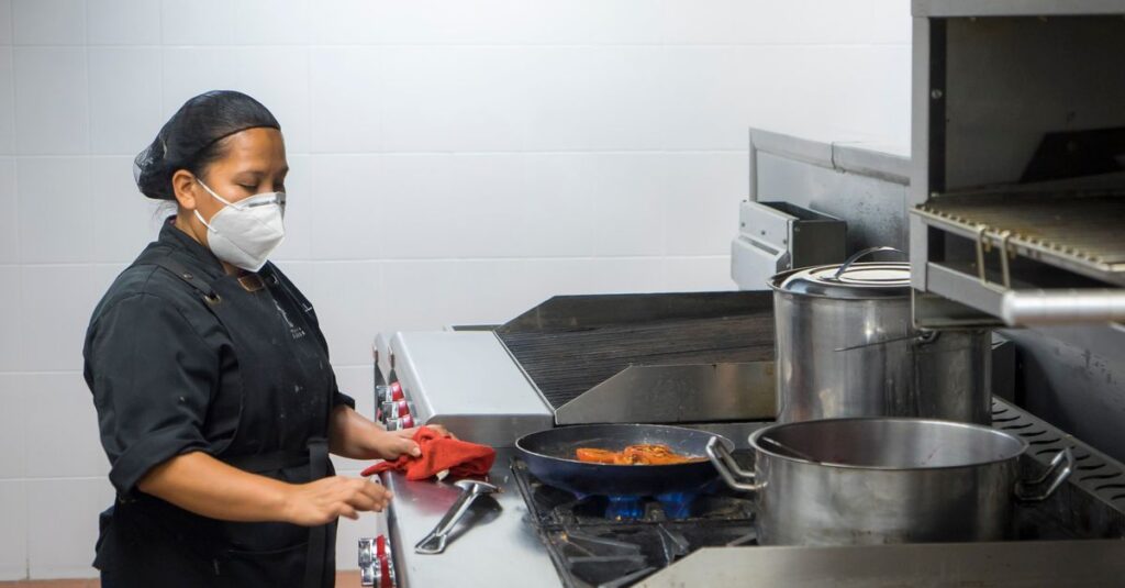 Chef busy at work in a commercial kitchen, preparing dishes while wearing a protective mask.
