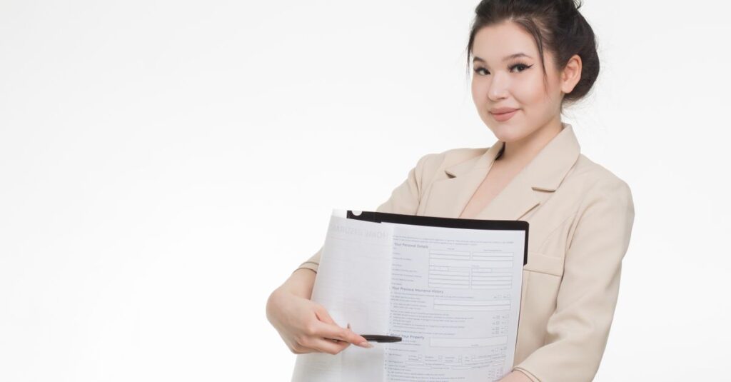 Smiling businesswoman in beige blazer holding and pointing to documents against white background.