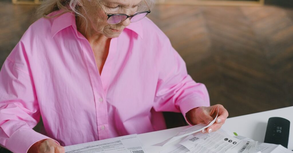 Elderly woman in pink blouse reading documents at a table indoors.